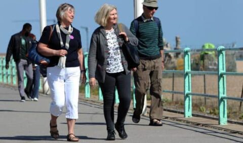 Older friends (including 2 women and a man) walking along a beach promenade