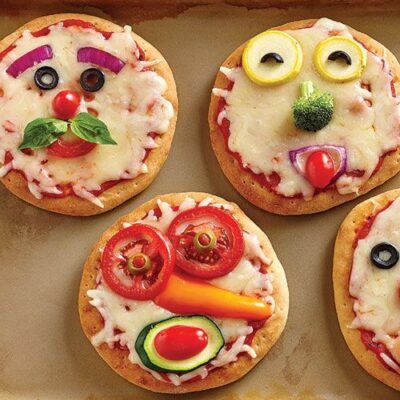 A range of small pizza with silly expressions drawn in veggies