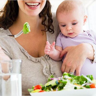 Mother eating a salad holding baby