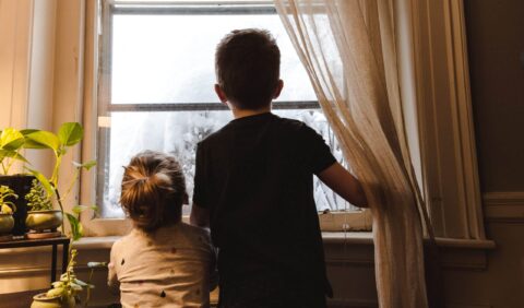 Two children looking outside a window from their house