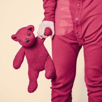 Child in red pajamas holding a red teddy bear