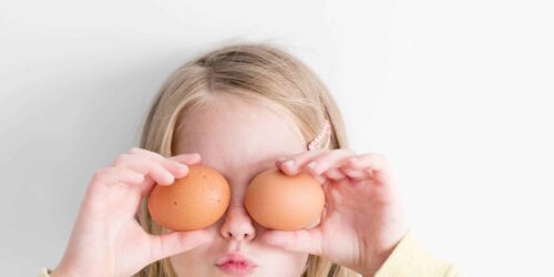 Young girl holding 2 eggs in front of her eyes and making a silly face