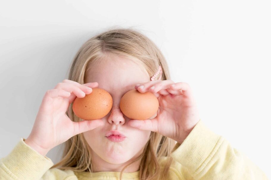 Young girl holding 2 eggs in front of her eyes and making a silly face