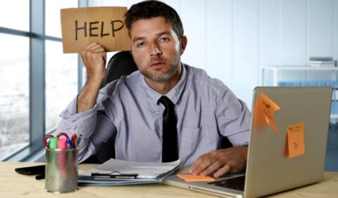 Stressed man in an office with a sign asking for help