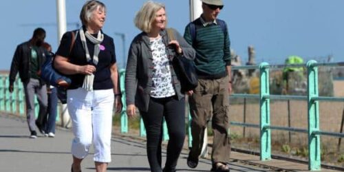 Older friends (including 2 women and a man) walking along a beach promenade