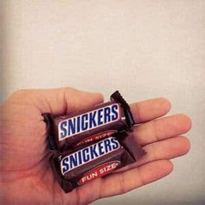 Two very small snickers bars held in a small hand for scale