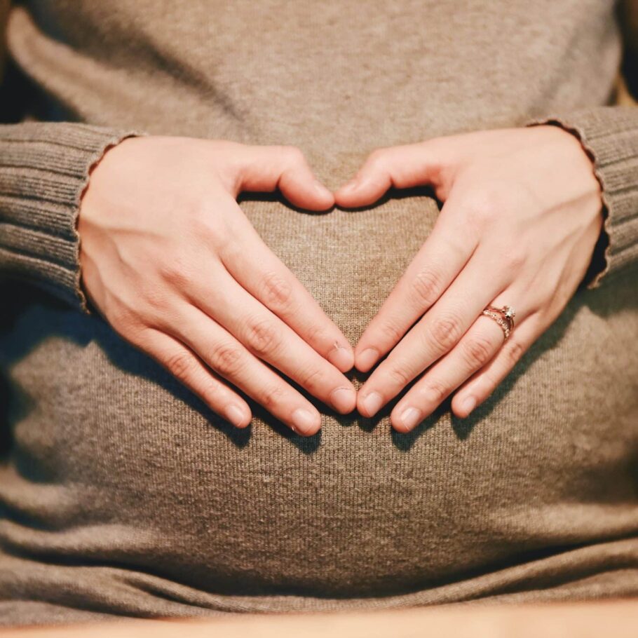 Pregnant woman forming a heart with her fingers over her clothed belly