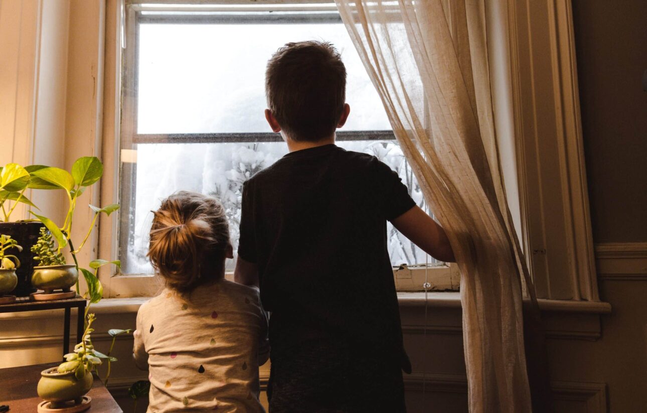 Two children looking outside a window from their house