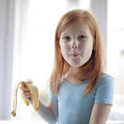 Positive cute little girl eating banana at home