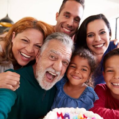 Multi-Generation Hispanic Family Taking Selfie To Celebrate Granddaughters Birthday At Home